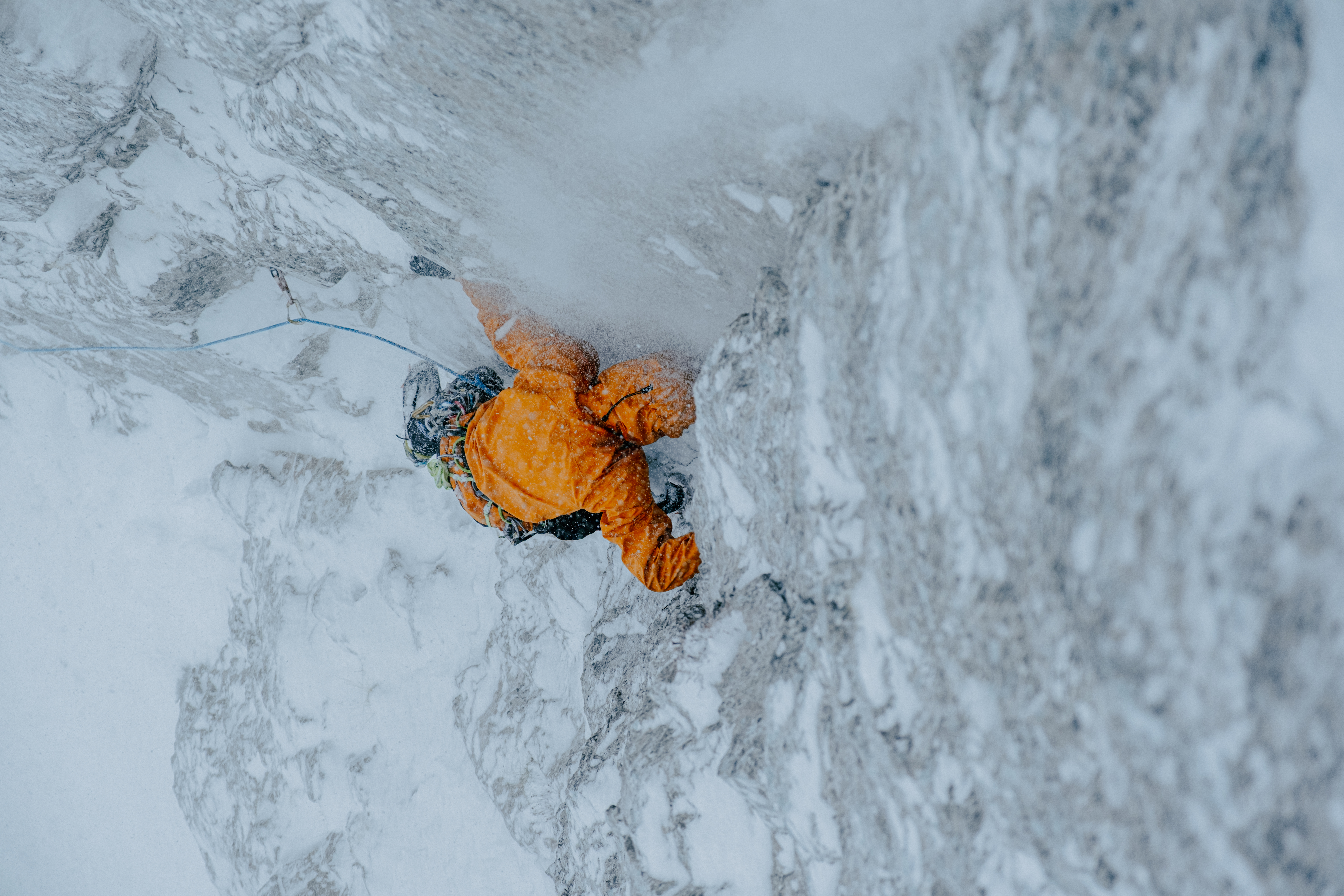 a climber navigates an icy climb wearing an orange arcteryx sperro sv jacket